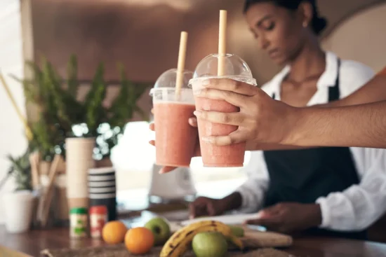 Businesswoman serves pink smoothies to customers at a vibrant juice bar filled with fresh fruits.
